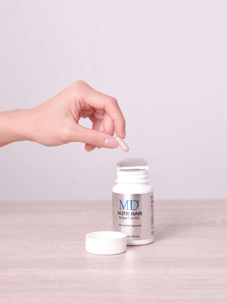 Hand taking a single MD Nutri Hair capsule from bottle – daily supplement for thinning hair and hair loss support